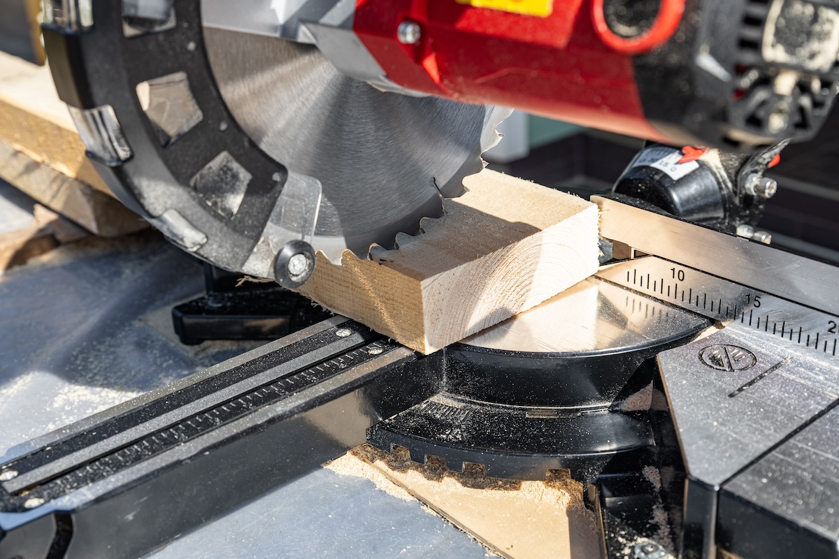 A red miter saw cuts a wood plank precisely.