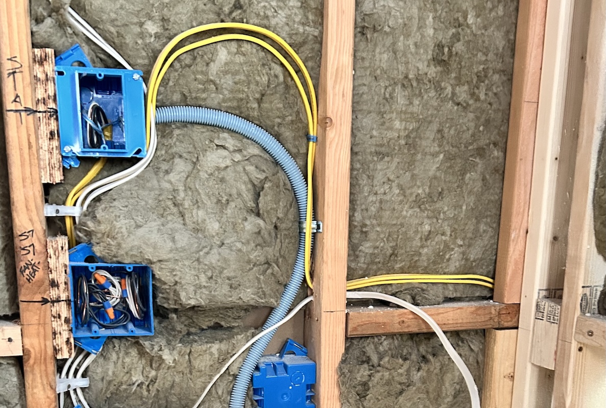 Unfinished wall with wood framing, insulation, and electrical work revealed.