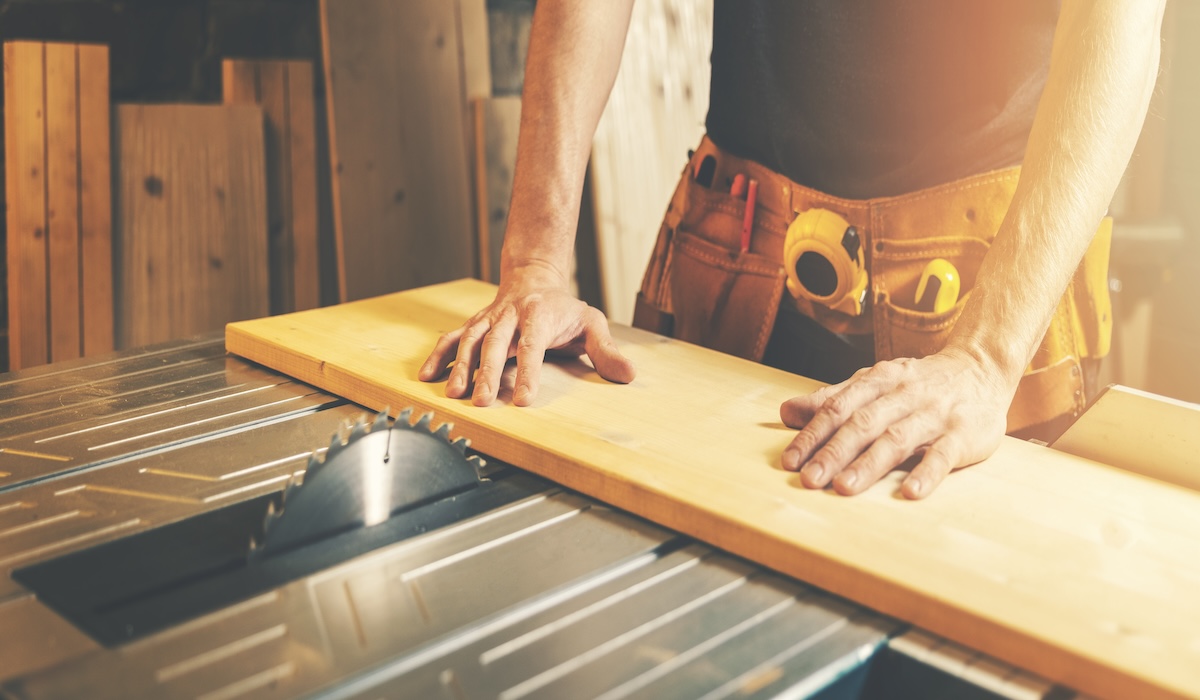 A woodworker pushes a wooden plank under a table saw.
