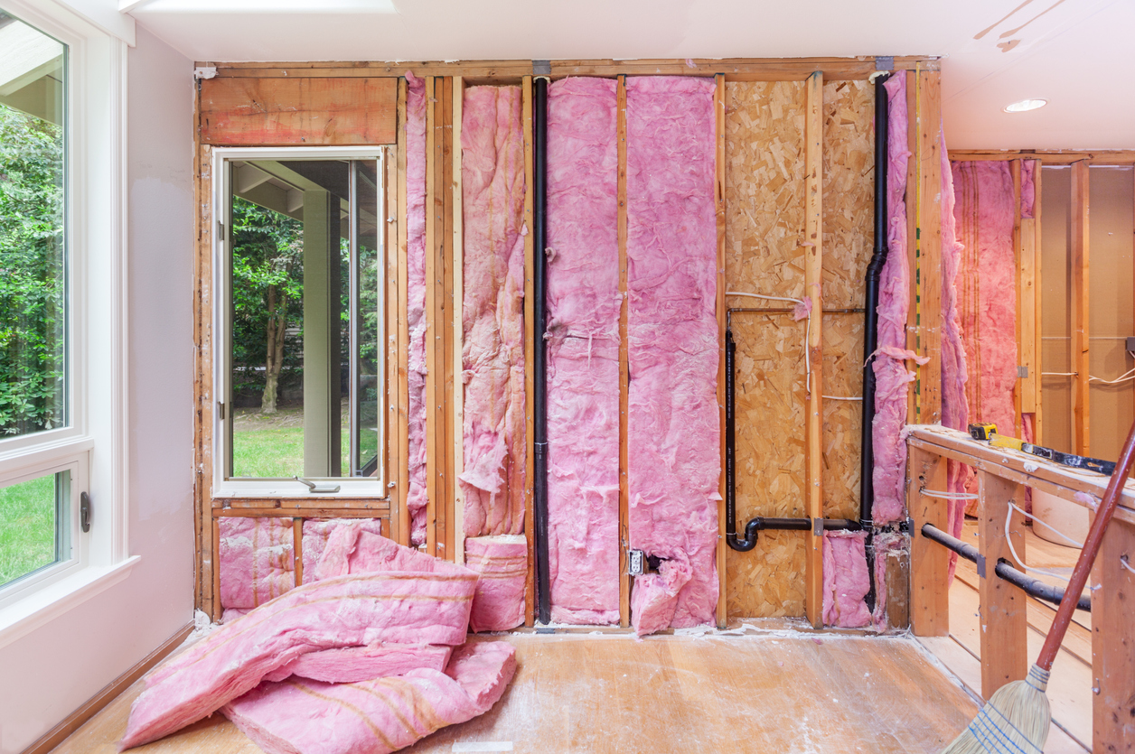 Interior room of home with no sheetrock on walls, and exposed insulation and studs.