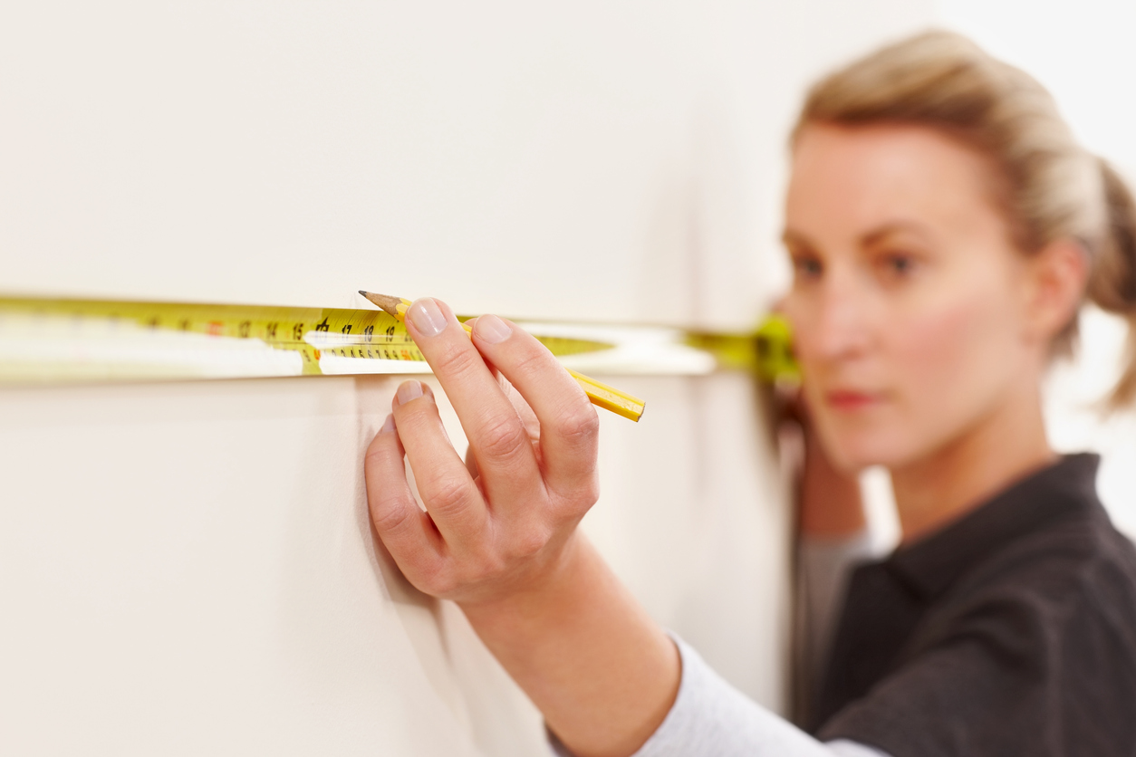 Woman using a tape measure to measure wall 16 inches from corner.