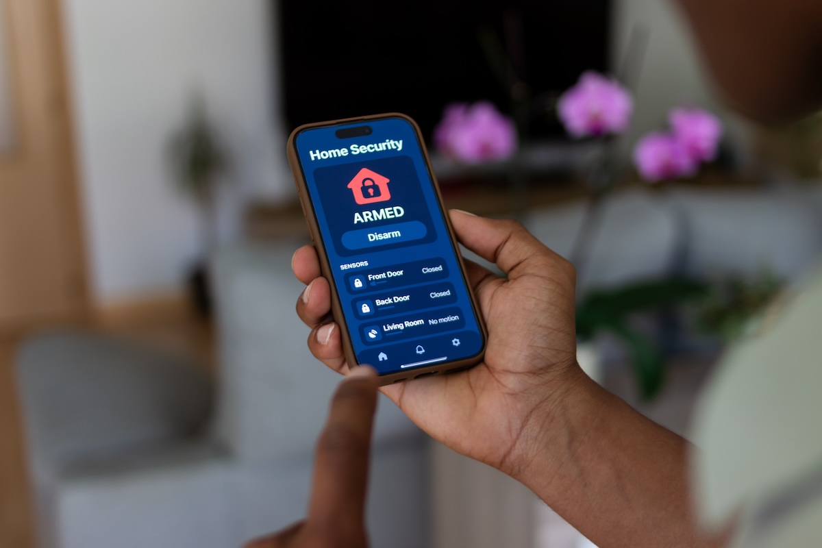 A person holds their smart phone to monitor their home security settings remotely.