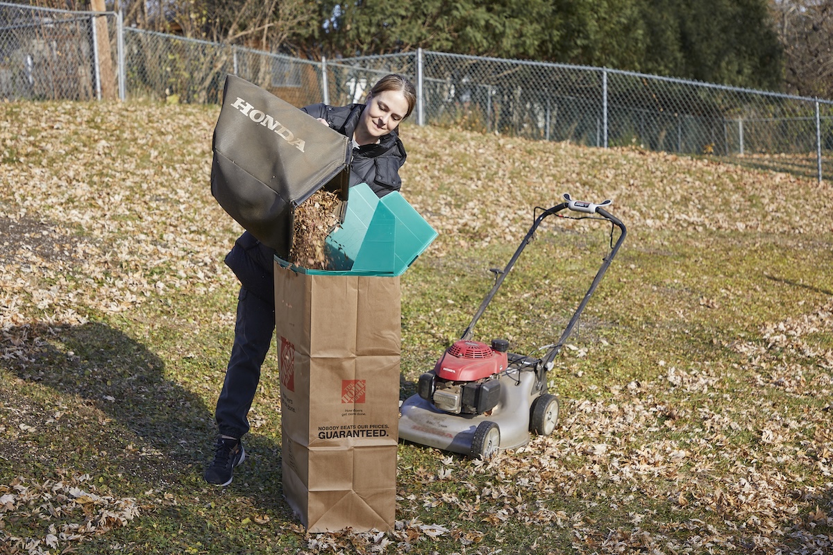 Woman dumps lawn mower leaf collecting bag into a brown yard refuse bag.