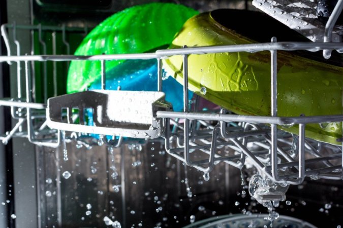 Colorful dishes in the top rack of a dishwasher are wet.