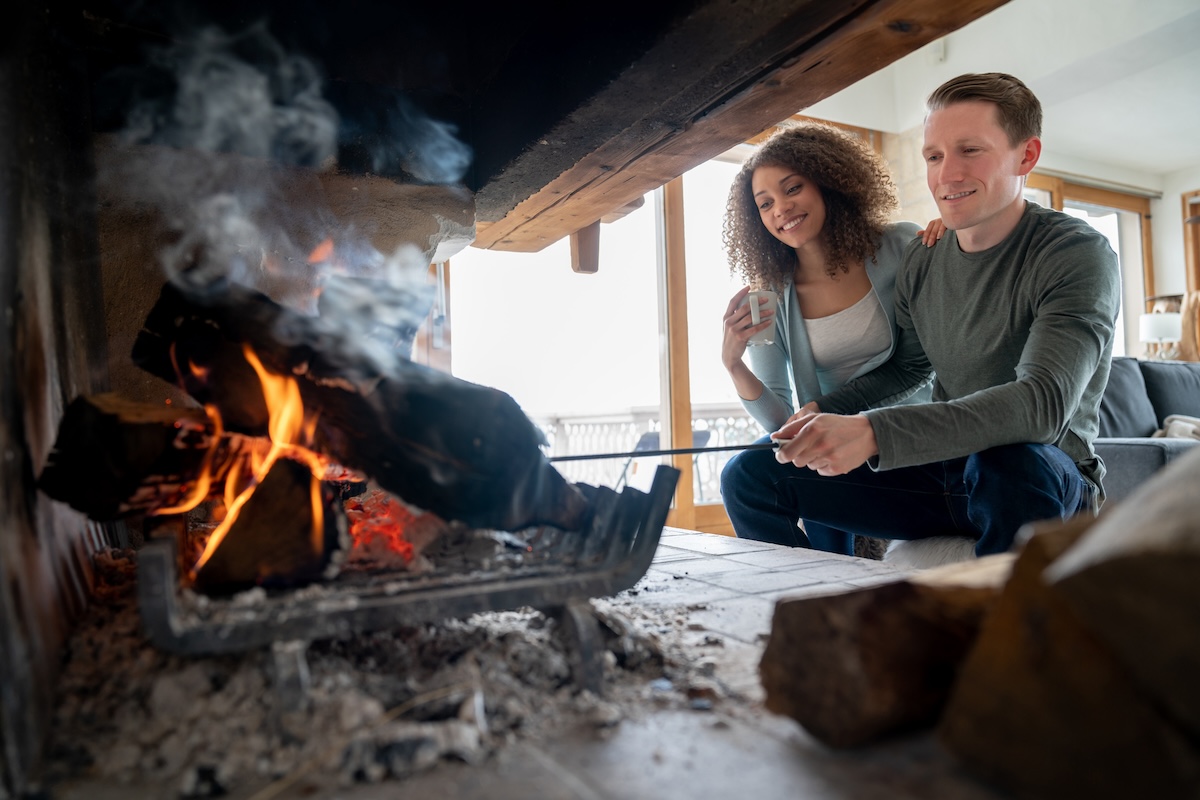 A young couple sits in front of an indoor fireplace.