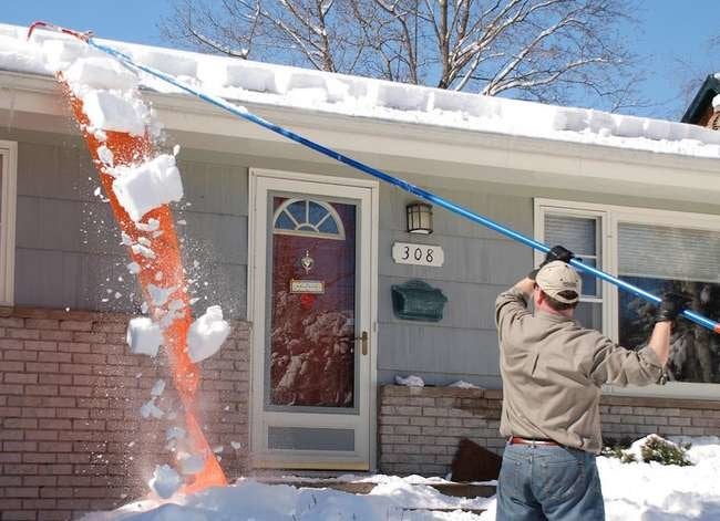 Person removing snow from roof with roof rake