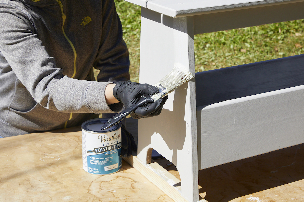 Woman paints a coat of polyurethane over a bench painted with chalk paint.