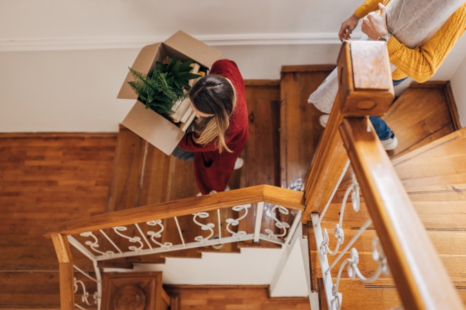 Man and woman carrying boxes and household items down a staircase.