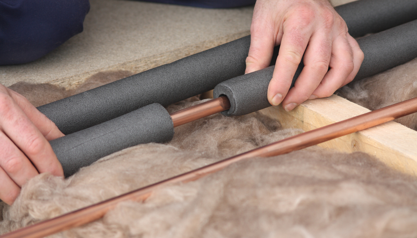 Man wrapping copper pipes with grey foam insulation.