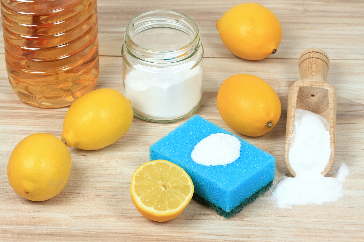Lemons, salt, baking soda, and a blue sponge on light wood