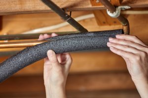 A person is adding insulation to water pipes.
