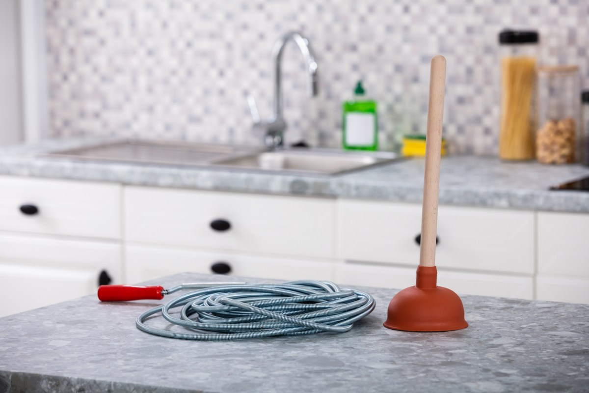 The best drain snake option sitting on a counter next to a plunger with a sink in the background