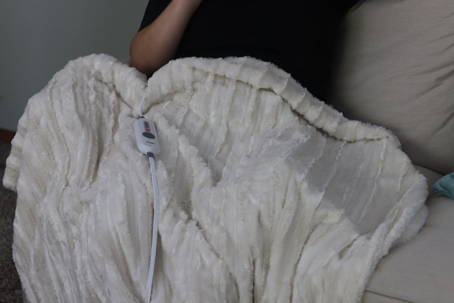 A soft-looking electric blanket and its controller on a person's lap.