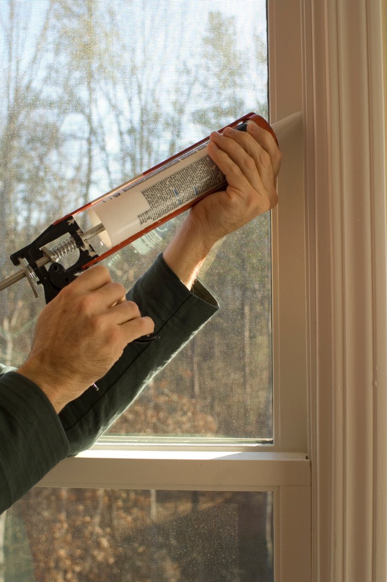 Person caulking window frame with a caulking gun.