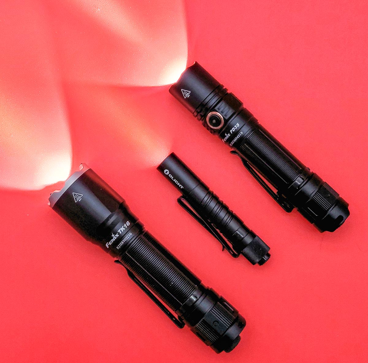 Three of the best flashlights with their lights on while sitting on a red background.