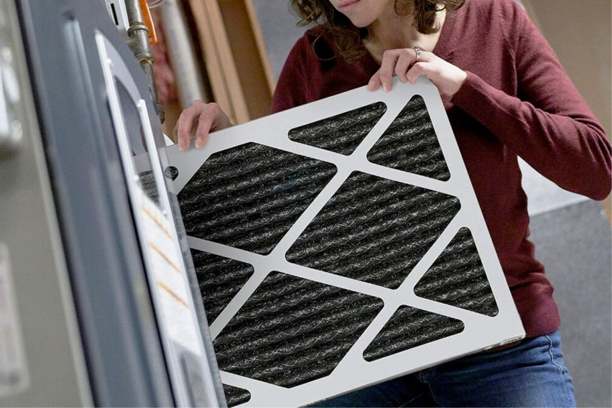 A person sliding a filter out of a furnace before replacing it with a new one.