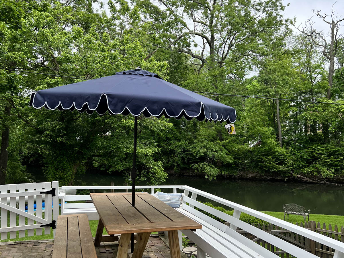 The best patio umbrellas option set up through a picnic table on a deck that overlooks a green grass yard bordered by large trees