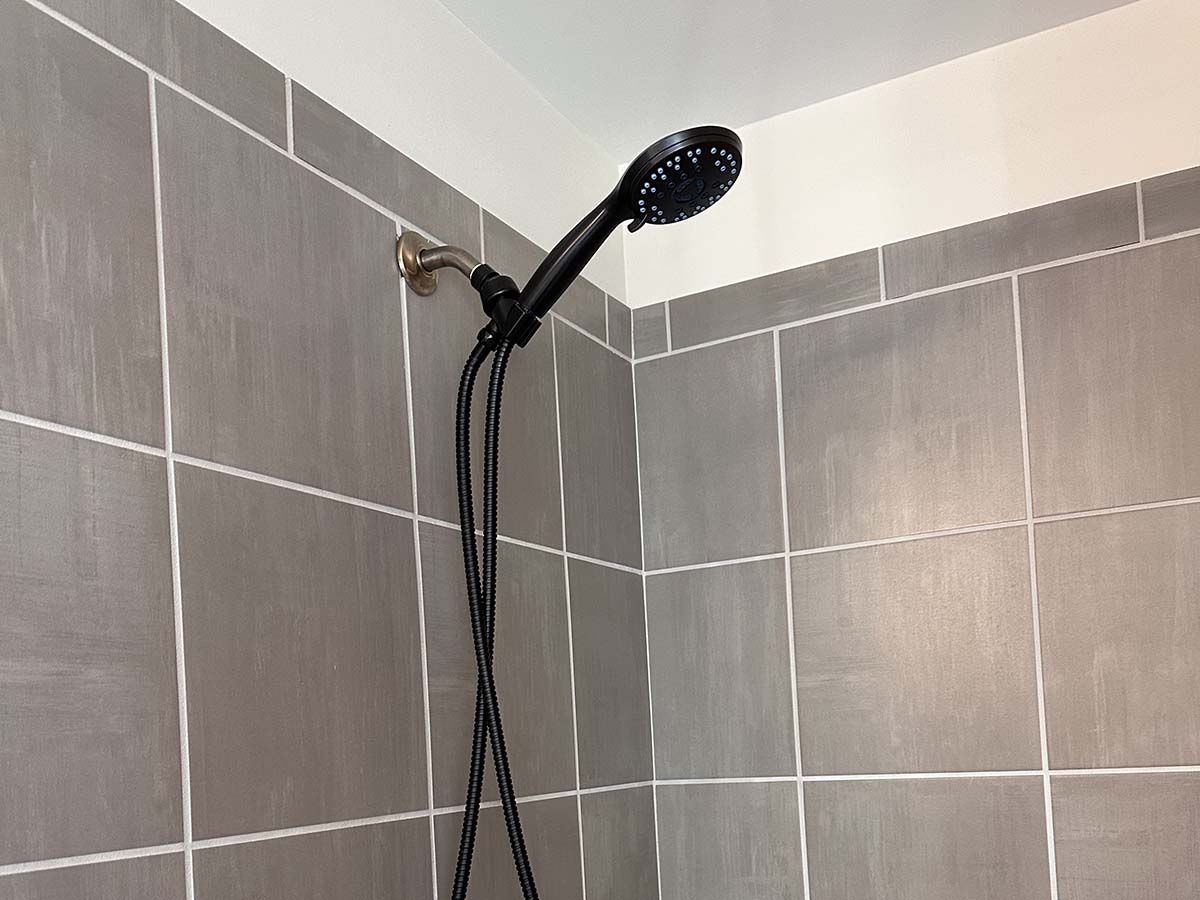 Matte black shower head mounted on large-scale square taupe tile