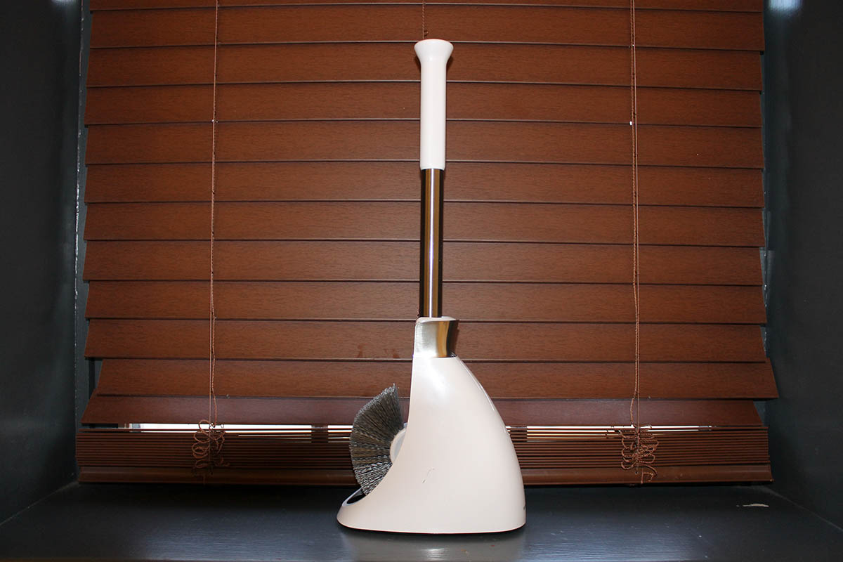 The Simplehuman Toilet Brush With Caddy on a counter in front of a window with its blinds closed.