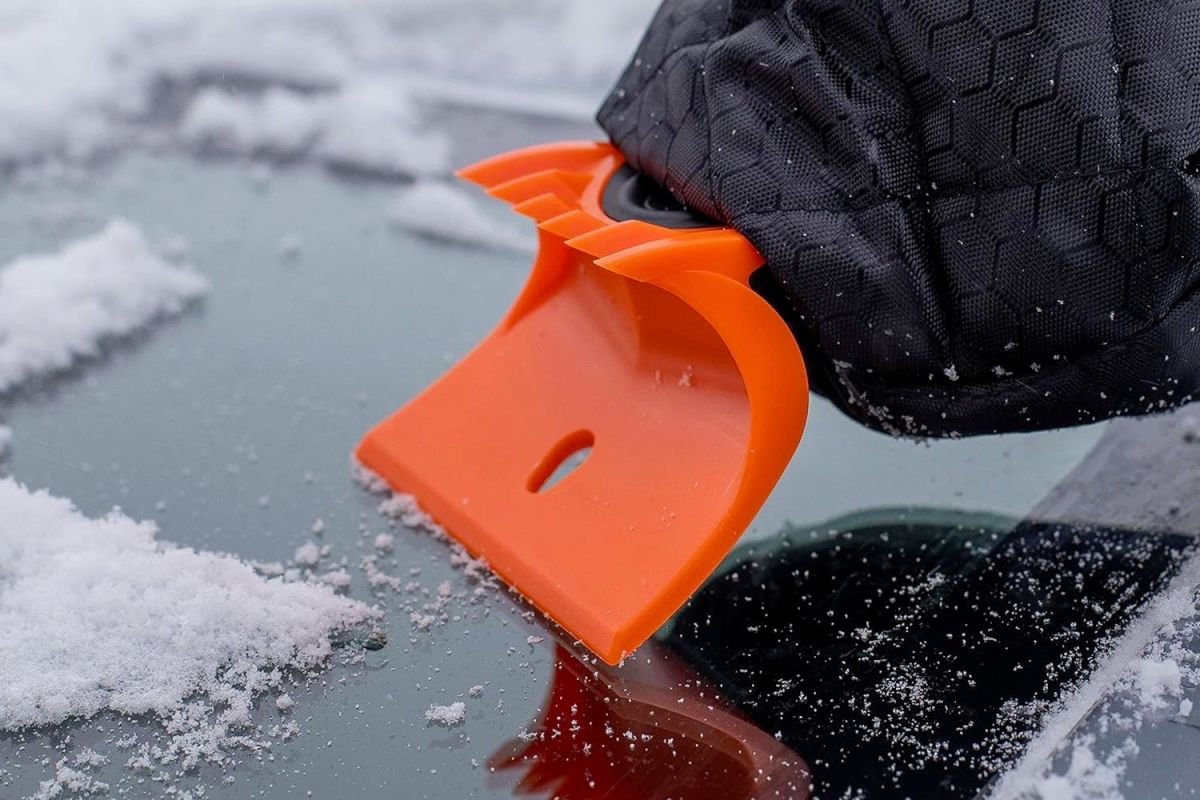 A person wearing a mitten and using the best ice scraper to clear a snowy and icy windshield.