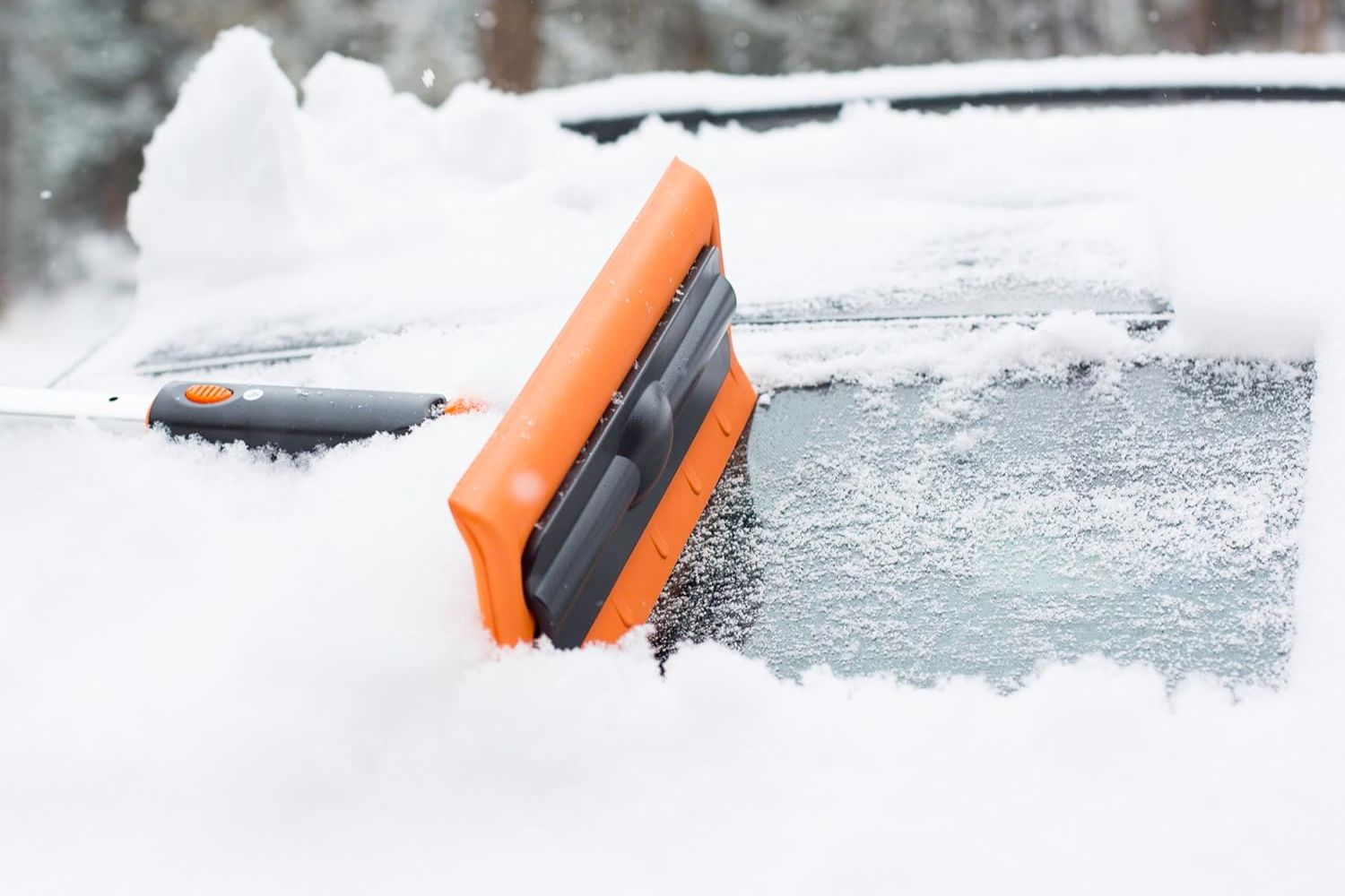 A person using the best ice scraper to remove snow and ice from a car's windshield.