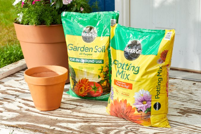 Bags of both potting soil and garden soil, side by side surrounded by a few terra cotta garden pots.