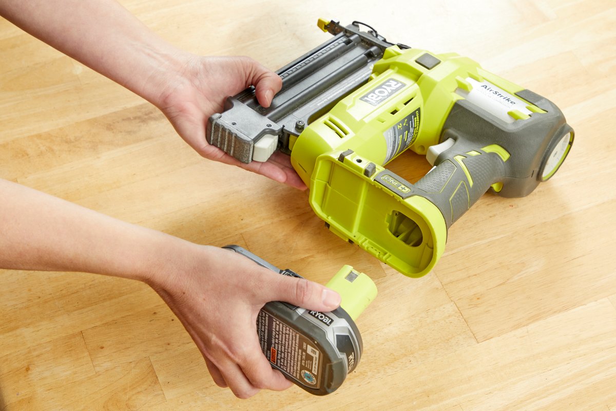 Woman inserts tool battery into a Ryobi nail gun.