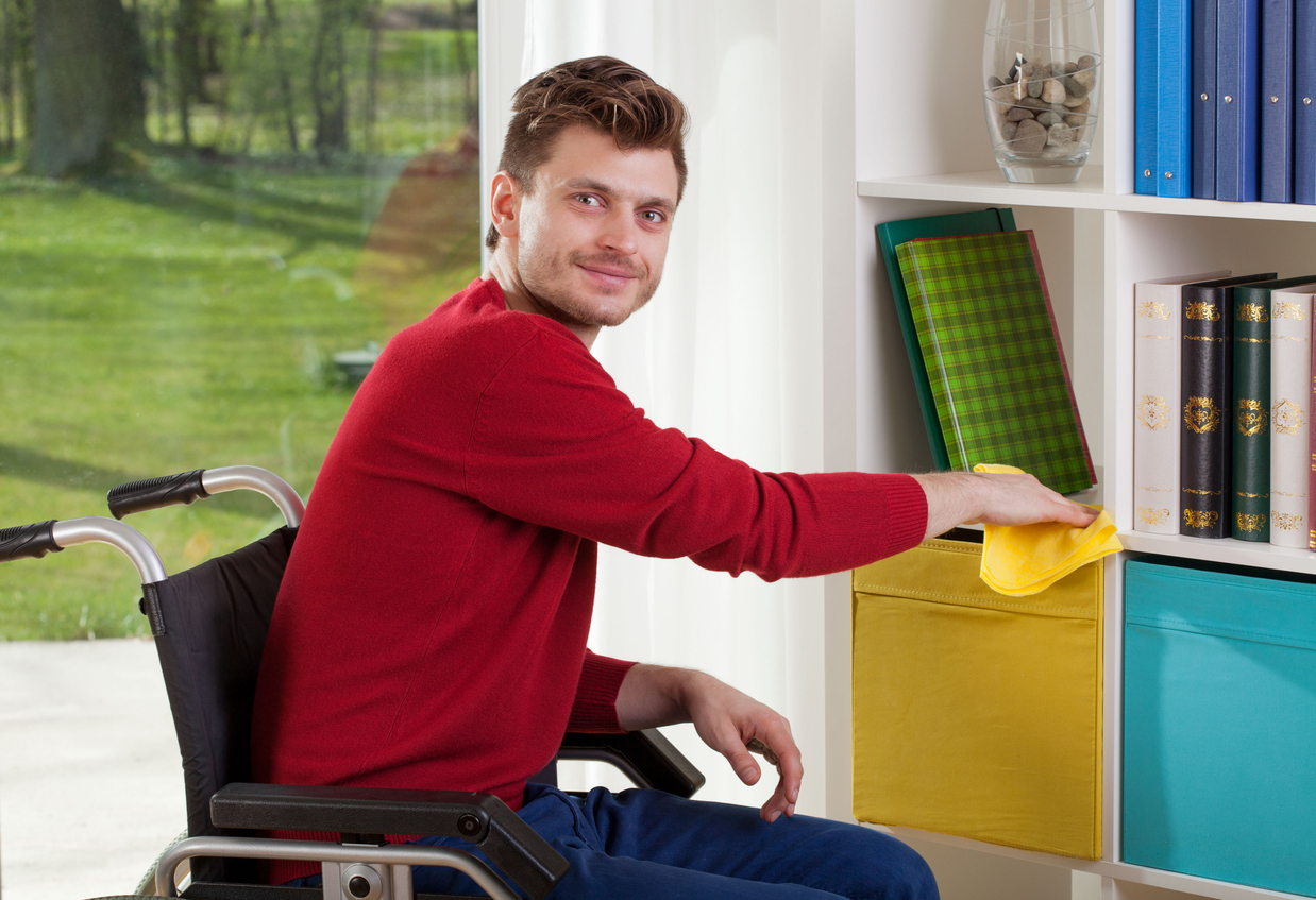 Man in wheelchair dusting shelves at home