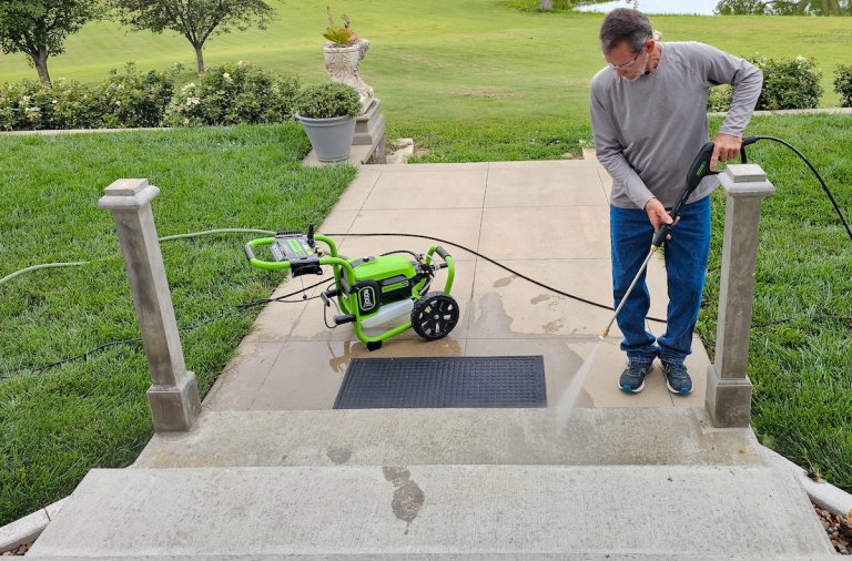 Man pressure washes the front walkway and steps of a home; image looks out toward walkway and front yard.