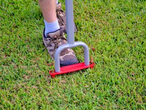 A person stepping on the Yard Butler Manual Lawn Coring Aerator during testing