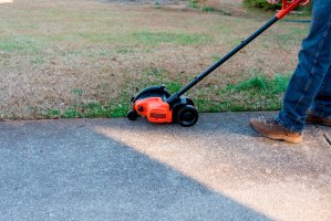 A person using the best lawn edger option to tidy a lawn border next to a driveway