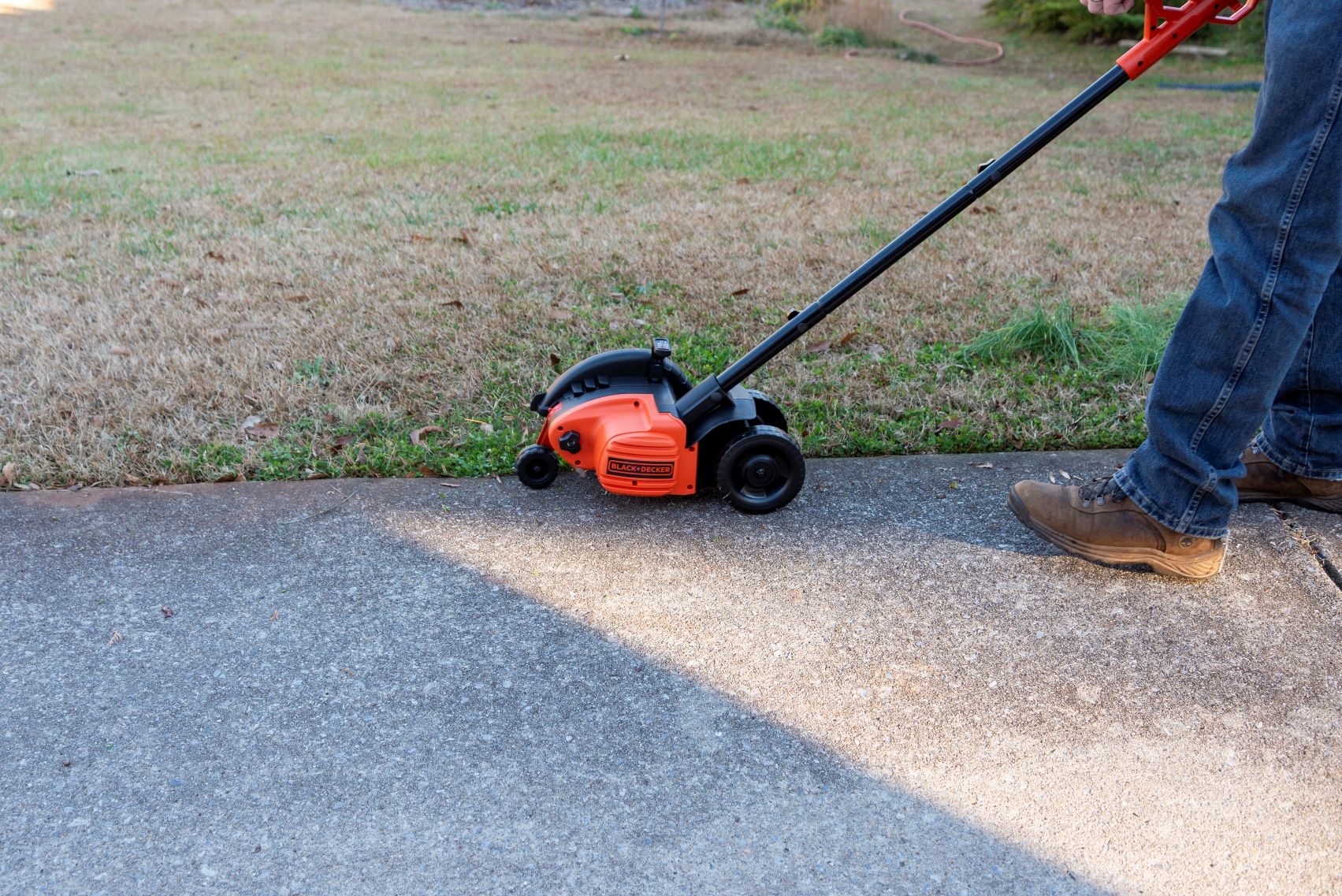 A person using the best lawn edger option to tidy a lawn border next to a driveway