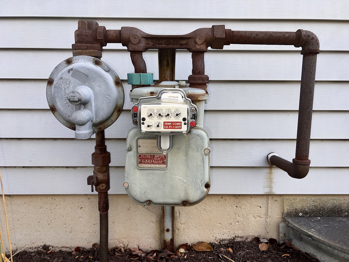 A natural gas meter on the exterior of a home with grey siding.