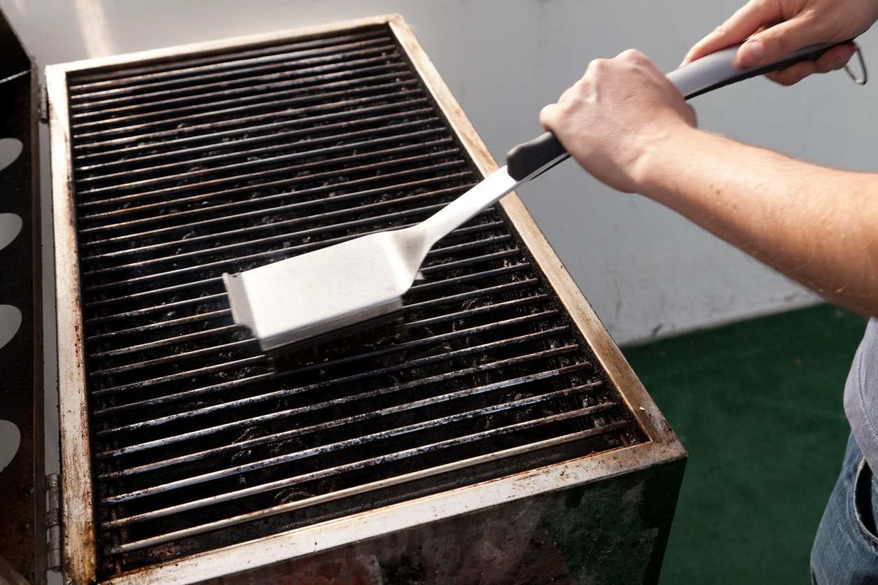 A person using the best grill brush option to clean the cooking grates of a grill