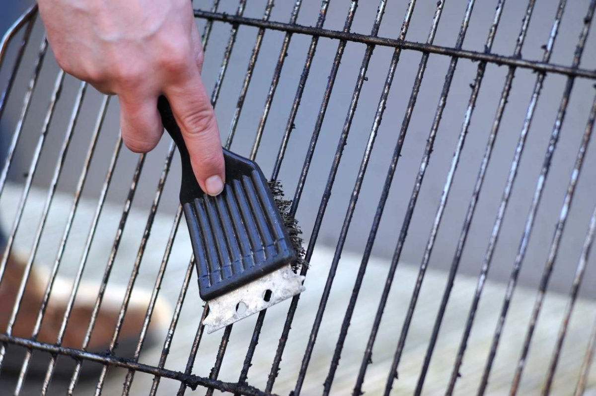 A person using the wire bristles on the best grill brush to clean grill grates.