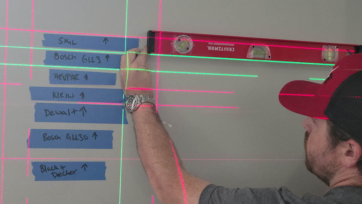A person using a traditional level to check the accuracy of several of the best laser levels during testing.