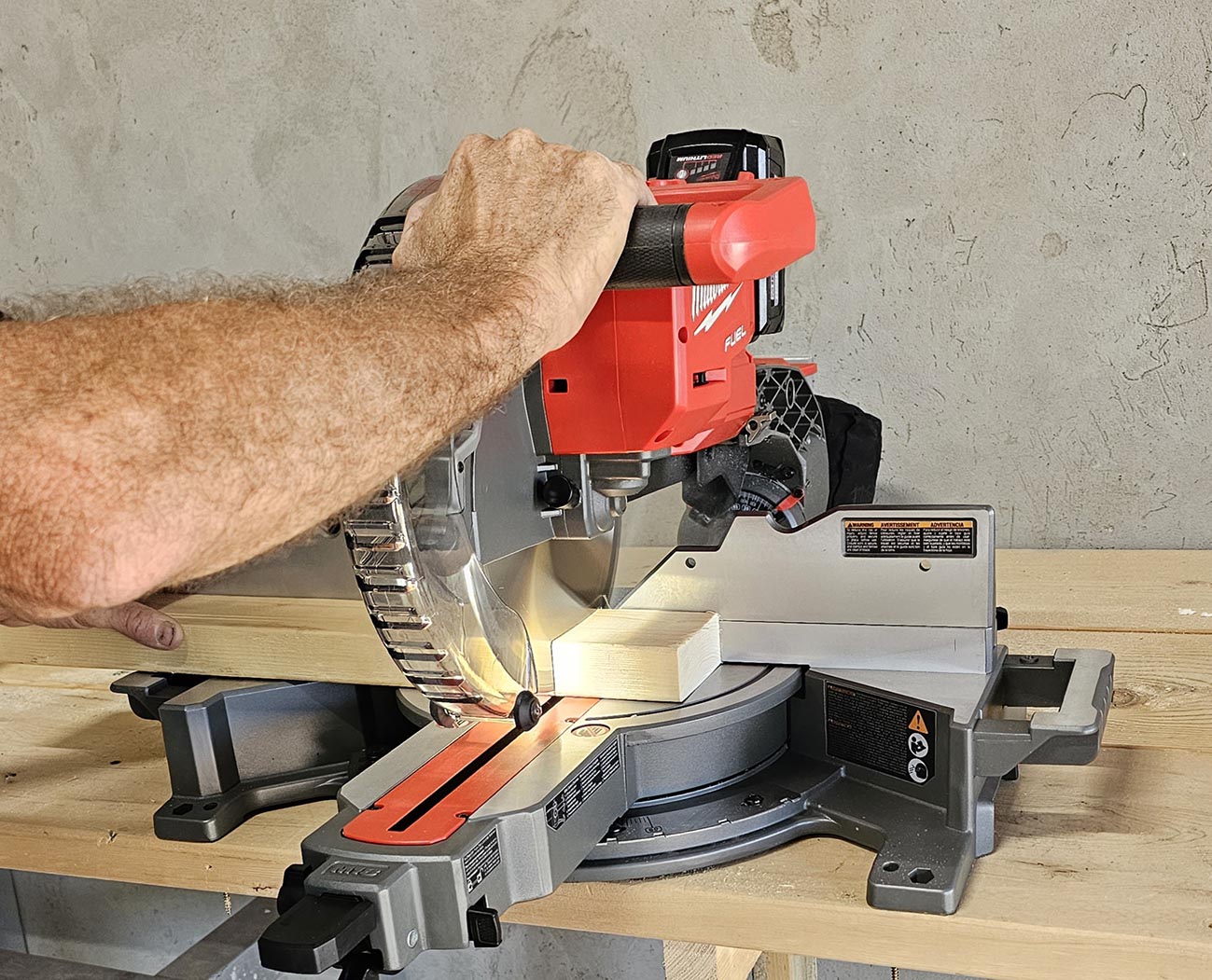 Contractor using a red Milwaukee 10-inch compound sliding miter saw to cut a 2 by 4.