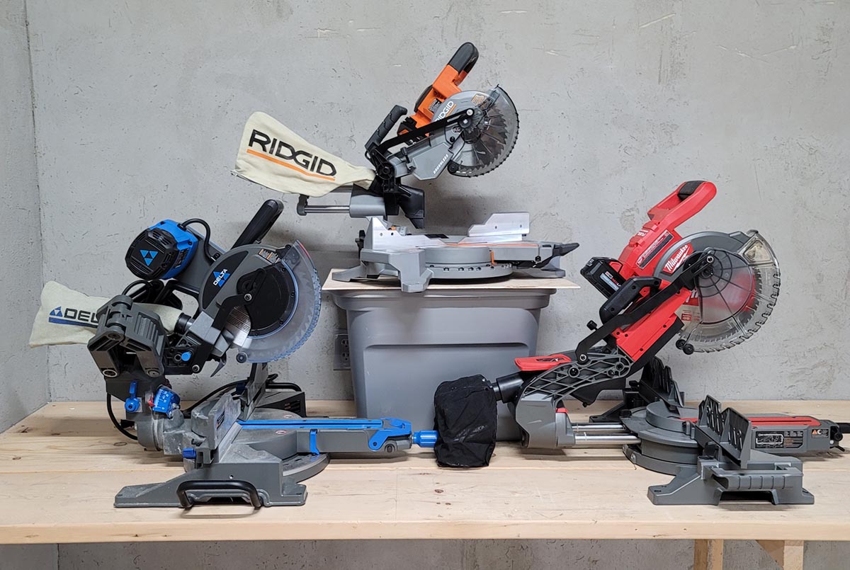 Three of the best tested miter saws on a workbench in front of a cement wall
