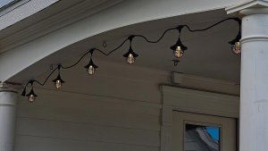 Black lantern-style Outdoor String Lights hung on the white overhang of a front porch