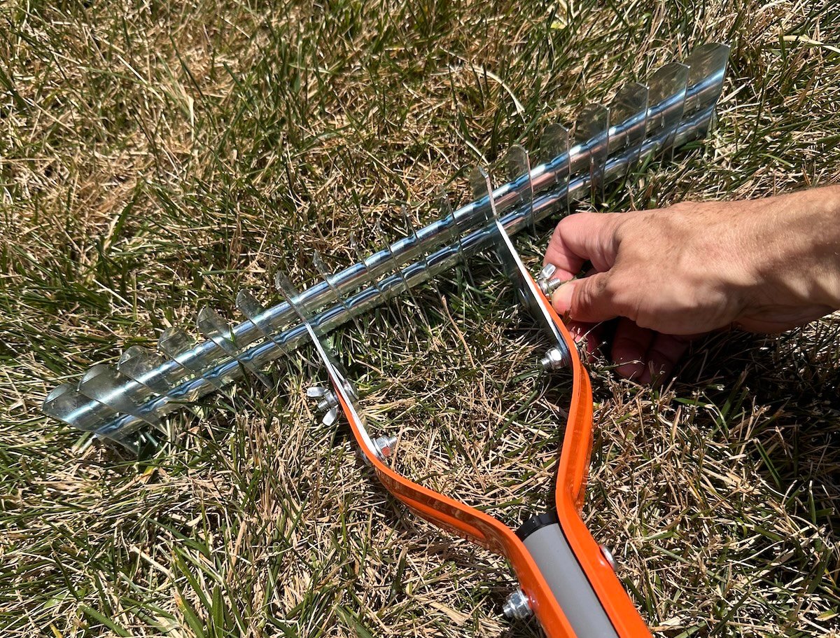 Man's hand adjusts a screw on the head of a manual dethatching rake.