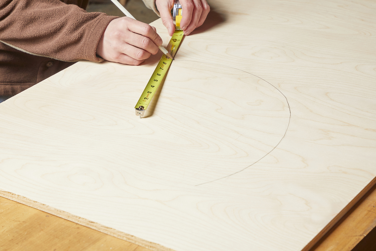 Person uses a tape measure hooked to a nail to draw a perfect circle on wood.