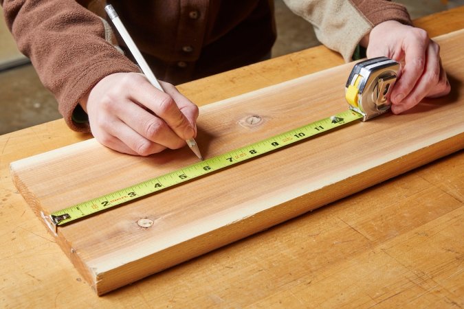Person wearing brown jacket holding a pencil uses a tape measure to measure a board.