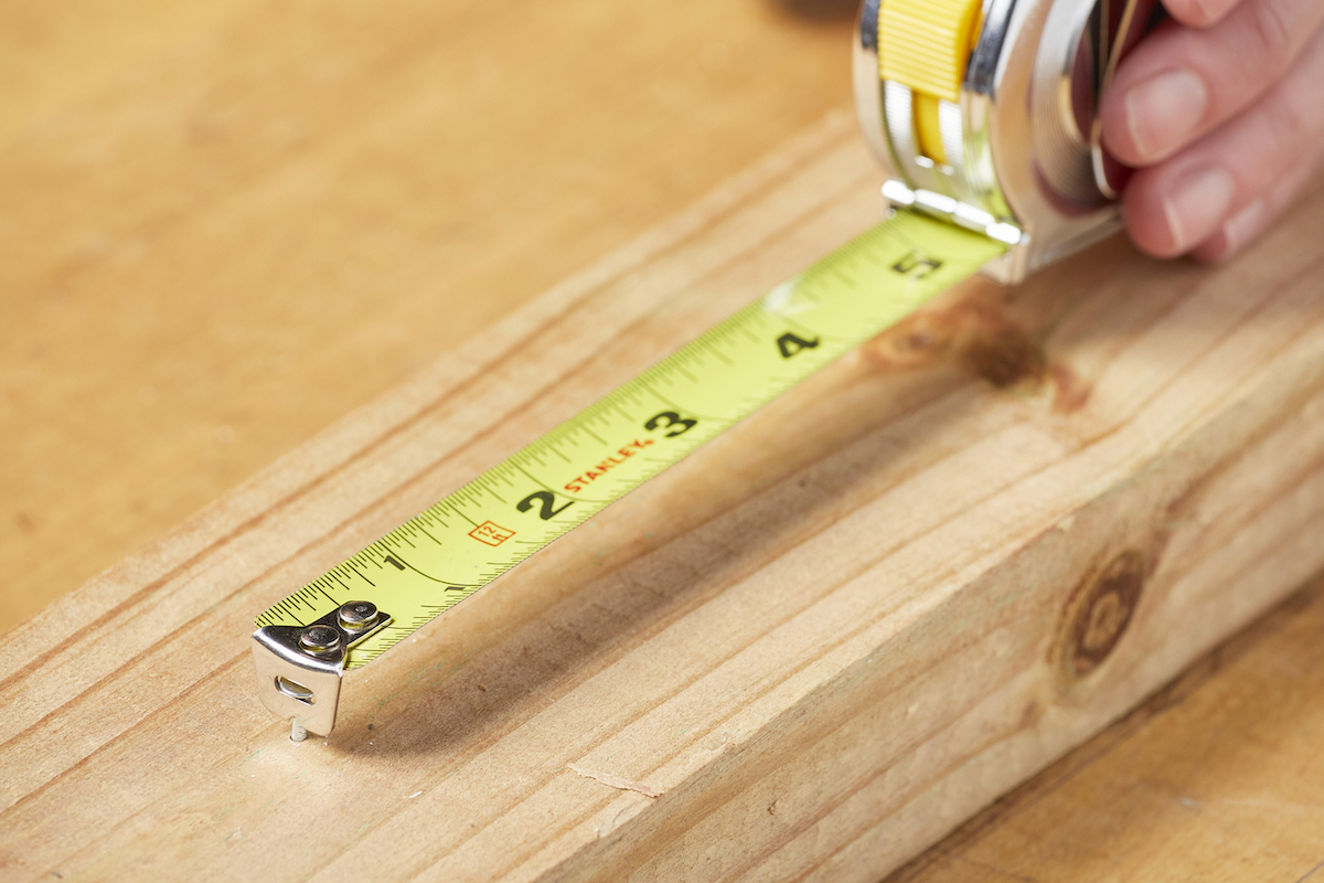 Tape measure tang hooked onto the a nail in a board.