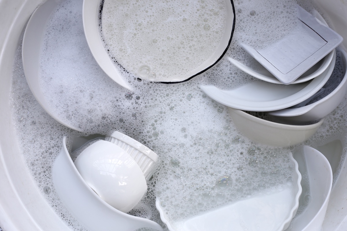 Many white dishes soaking in soapy dishwasher.