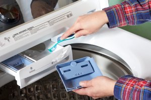 A person uses a toothbrush to scrub grime from a washing machine.
