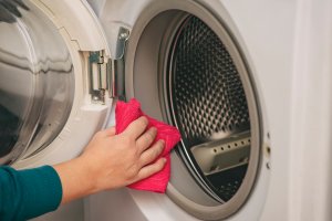 A person wipes a washing machine with a pink towel.