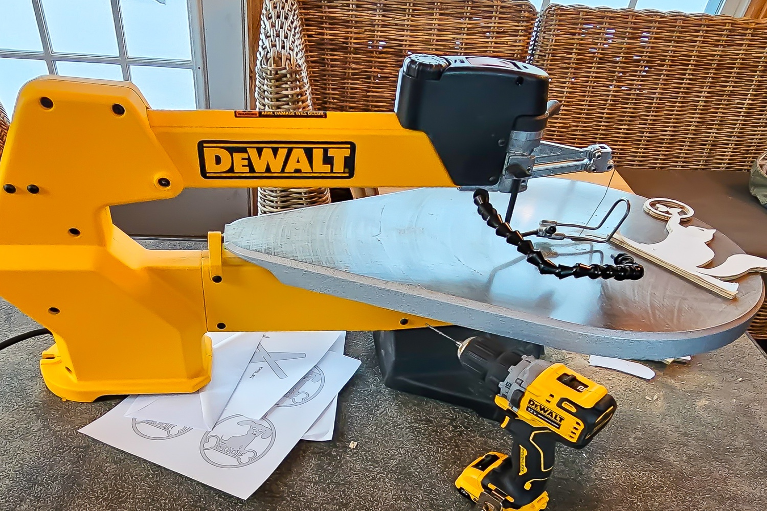 The DeWalt 20-Inch Variable-Speed Scroll Saw set up on a workbench with a drill and several patterns.