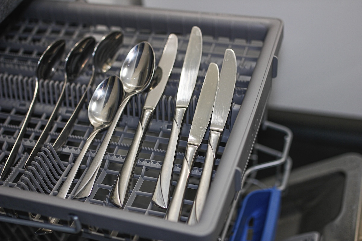 Spoons and butter knives in the top cutlery drawer of a dishwasher.