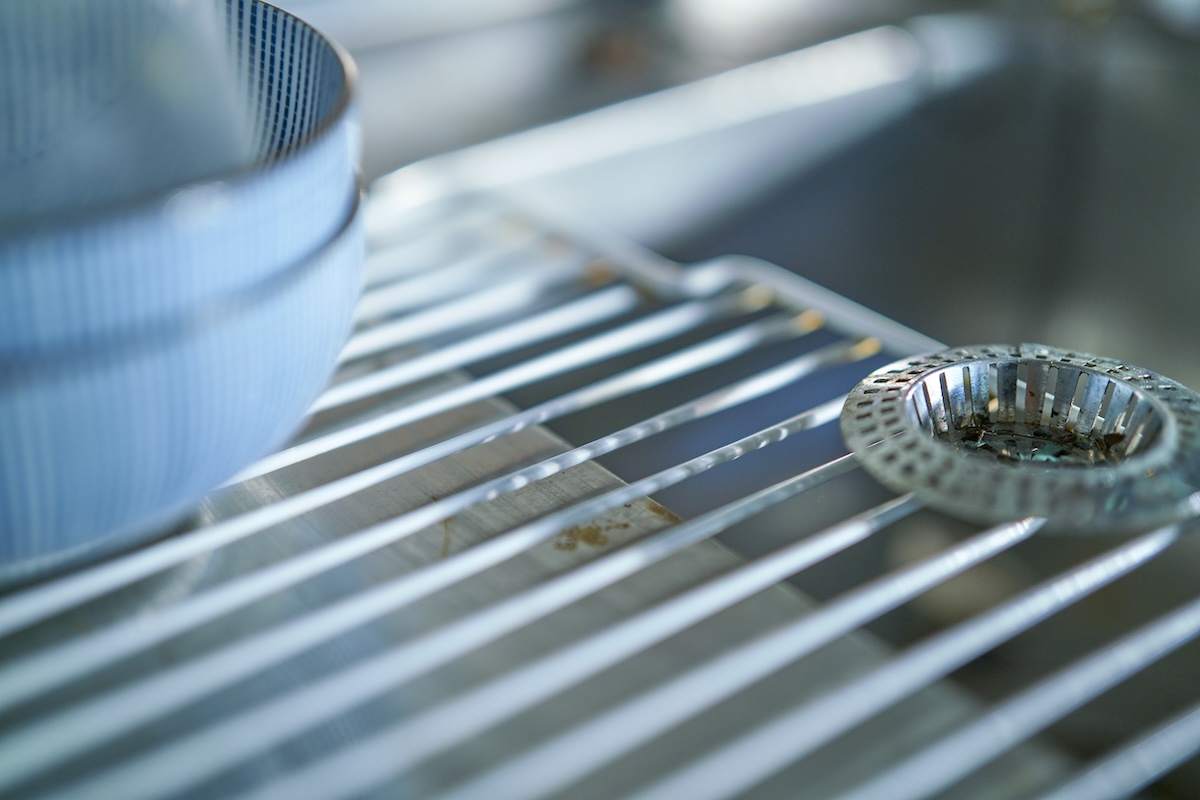 Close up of metal drying rack next to kitchen sink with blue bowl on top.