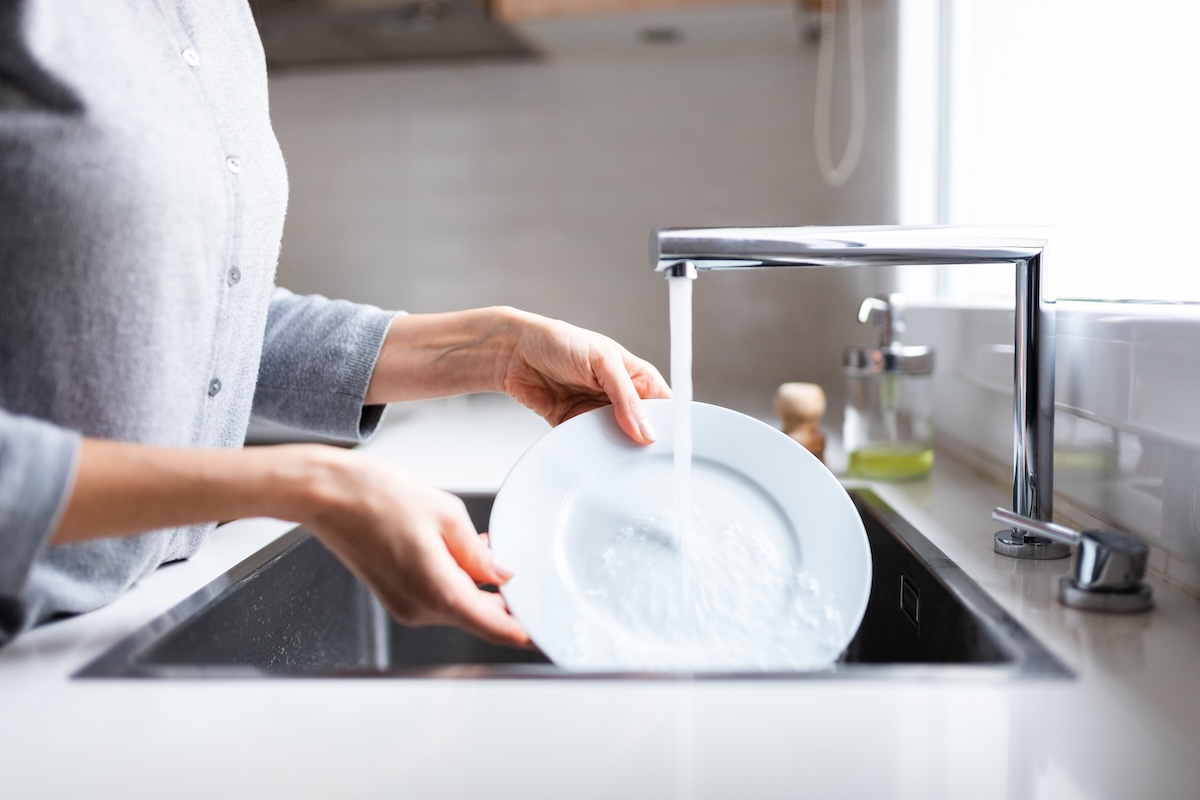 Close up of woman hands rinsing dishes in kitchen sink.